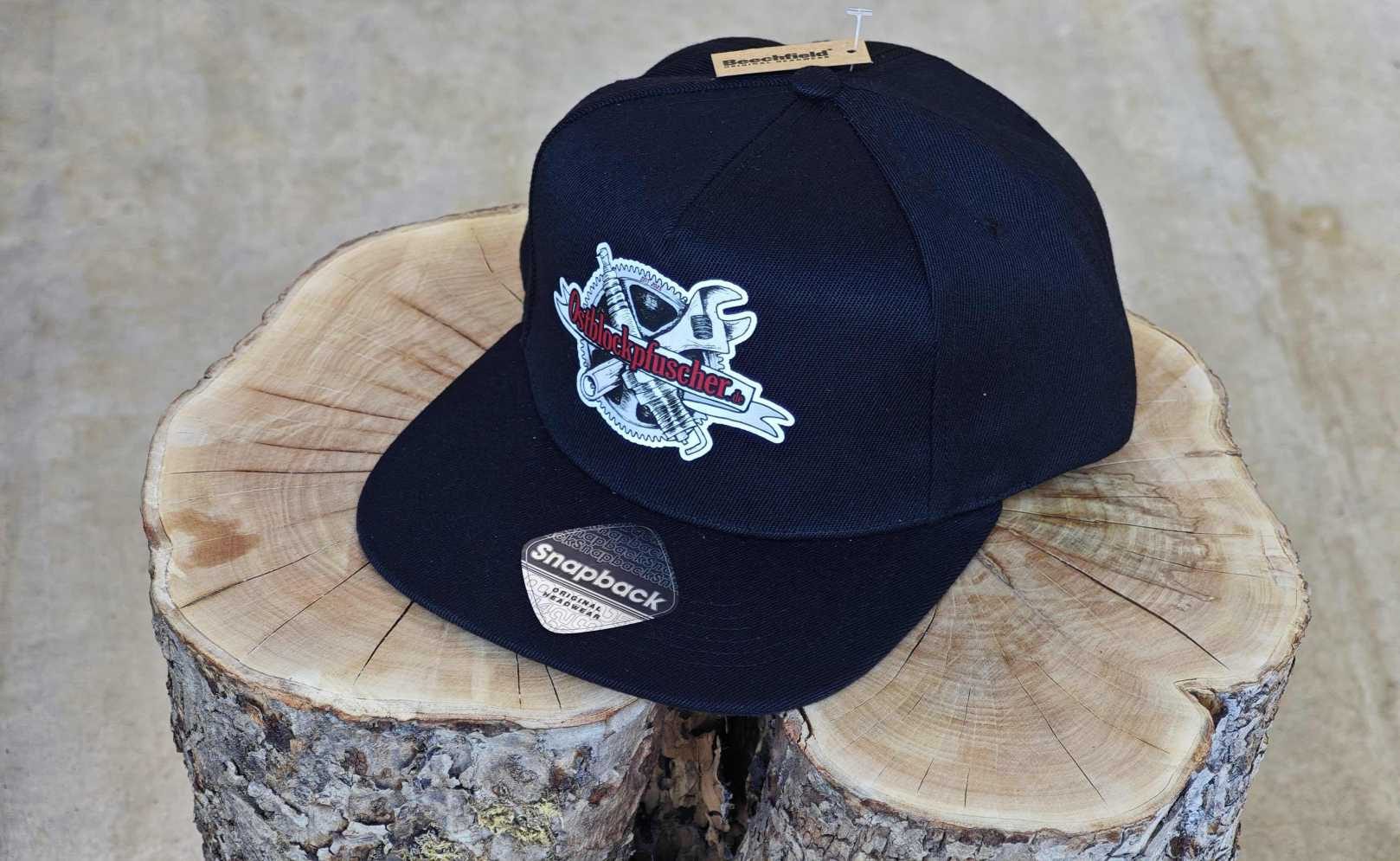 Cap mit gesticktem Ostblockpfuscher-Logo auf einem Holzstamm